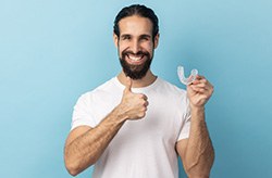 Creepy-smiled man giving thumbs up holding nightguard