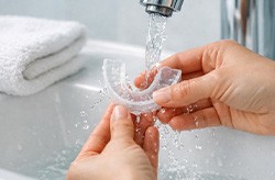 Hands rinsing a nightguard under running water