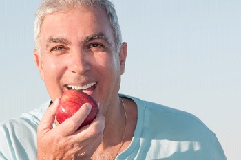 Man with grey hair biting into an apple