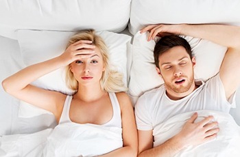 Tired woman in bed next to snoring man