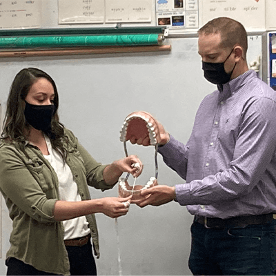 Dentist and team member demonstrating flossing on smile model