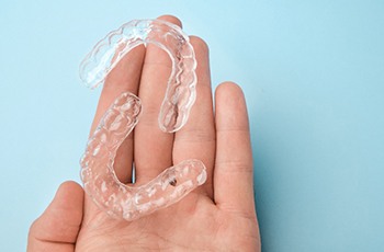 Patient holding clear aligners against blue background