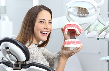 a patient smiling and holding a model of dentures