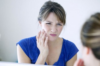 woman with dental implant pain wincing at her reflection in the mirror