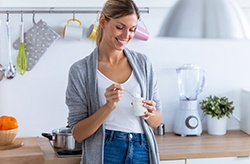 woman standing in her kitchen and eating yogurt 