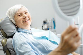 Woman smiling in the dental chair after receiving dental implant supported dentures