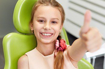 Child in dental chair giving thumbs up during children's dentistry visit