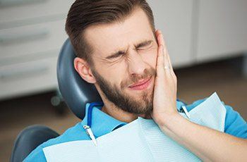 Man in dental chair holding cheek before emergency dentistry