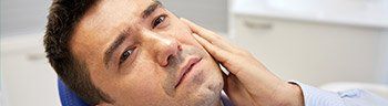 Man in dental chair holding jaw before oral surgery