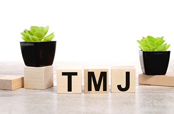 Wooden blocks spelling out “TMJ” between two plants