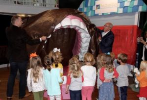 Dentists unveiling their exhibit to a group of children.