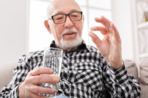 person holding a water glass and a pill