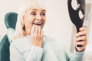 happy senior woman admiring new teeth in mirror