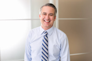 older man in blue shirt and tie smiling 