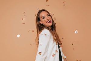 Woman wearing a white blazer smiling with gold confetti raining over her