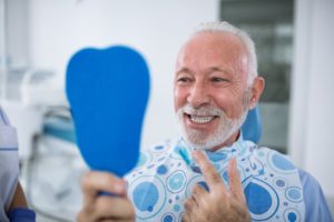 senior man admiring his smile in a mirror after getting dental implants in Columbia 