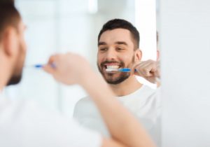 man smiling while brushing his teeth 