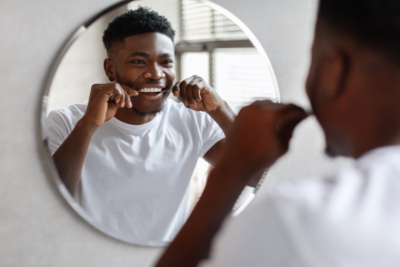 man flossing around his dental implants in Columbia