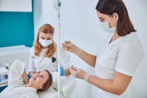 Woman in dental chair being assisted by a dentist while another dentist checks IV equipment