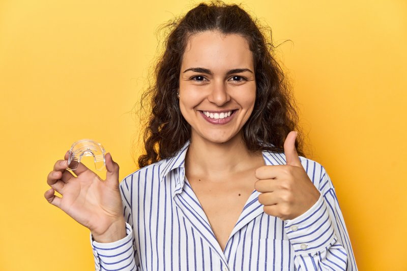 A woman smiling as she holds up her oral appliance