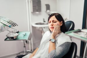 Young woman clutching jaw in pain sitting in the dentist's chair. 