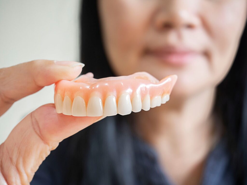 Woman in blue holding upper arch of dentures