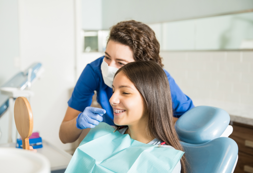 Teen in dental chair smiling while dentist points at their smile