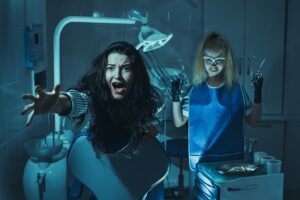 Scene from a scary movie: dental patient leaps out of chair in fear while scary staff member stands holding tools in hand.