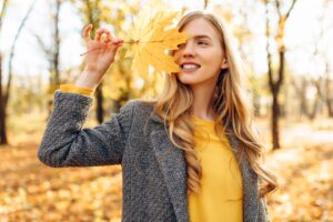 Woman outside in the woods smiling holding golden leaf to her face